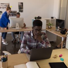 Side view of young African-American male executive working on laptop at desk in the modern office