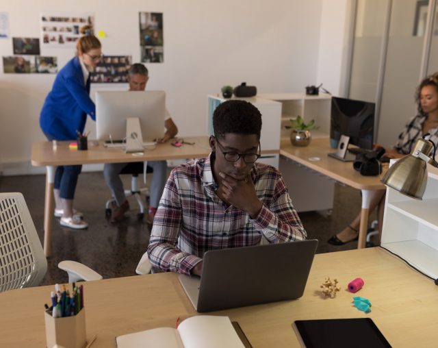 Side view of young African-American male executive working on laptop at desk in the modern office